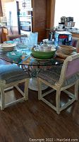 Glass top round dining table with metal base and four chairs, showing general condition and items on table.