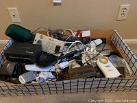 Box filled with various electronic items including phones, cords, clock, discman box