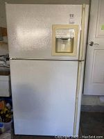 Full view of white GE Profile refrigerator with freezer on top and refrigerator on bottom, featuring a built-in water and ice dispenser on freezer door.