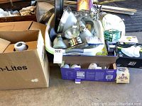 Plastic storage bin filled with assorted lighting hardware and fixtures alongside cardboard boxes with additional lighting parts.