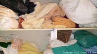 Photo of the two shelves with assorted folded linens and towels including white, beige towels and some blankets.