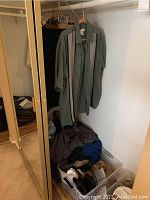 Photo of men's robes and shirts hanging on rack with bin of shoes and clothing piled below