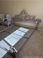 Full view of metal king size headboard and frame assembled on the floor against a wall, showing ornate design in metal.