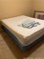 Photo of queen size mattress with protective sheet on top and folded sheets on mattress