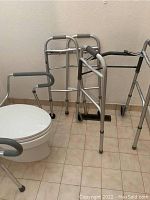 Two metal walkers and metal toilet safety frame arranged next to a toilet