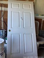 Photo of one white six-panel sliding door standing upright showing knob hole and minor surface wear.