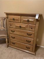 Front view of a wooden tall boy dresser with six drawers and ornate drawer handles, some drawer faces feature carved decorations.