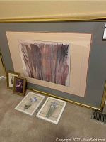 Large framed abstract watercolor style painting on wall with two small framed pictures and two white-framed floral paintings on the floor