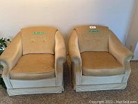 Front view of two matching beige accent chairs with cushioned seats and backs, showcasing their size and shape.