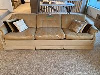 Front view of a tan upholstered couch with three seat cushions and eight assorted throw pillows of various colors and patterns.