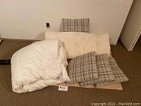 White Daniadown quilted duvet next to four plaid fabric throw cushions and a beige mattress pad on floor.