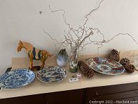 Overview of three plates, horse figurine, vase and pine cones on surface