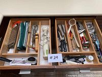 Two wooden kitchen drawers with dividers holding various kitchen utensils including knives, graters, mixer, and corkscrews.