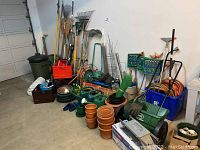 Wide overview of all items against a garage wall, showing tools, pots, hoses and cages