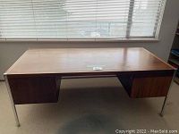 Front view of large wooden office desk with two drawers and metal legs under a window