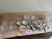 Full view of all items including glass bowls, plates, tea cups and saucers, cutlery, and candle warmer arranged on brown paper