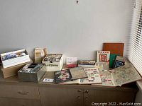 Wide shot of multiple stamp albums, loose stamps, and envelopes on top of a cabinet showing variety of stamp collections and books