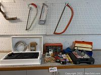 Multiple hand saws hanging on pegboard, tool boxes and containers with hardware and fasteners, rolls of tape, sanding blocks with handles, and the Jenn Air grill heating element on countertop.