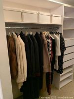 White shelf with four white fabric storage boxes on upper shelf and assorted women’s garments hanging on rod below