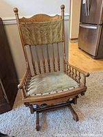 Front view of antique wooden platform glider rocker with upholstered seat and backrest showing the turned spindle design and natural wood finish.