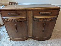 Front view of the wooden sideboard showing the curved front doors and carved fruit design drawer pulls on the two drawers above.