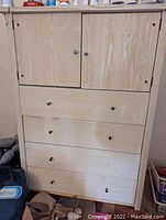 Front view of the solid wood dresser showing the pickled greige finish, two cupboard doors at the top, and three drawers below with metal knobs, one missing knob.