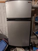 Front view of silver diamond plate Gladiator garage refrigerator freezer with top refrigerator door and bottom freezer door