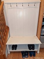 Full view of the white wooden mudroom bench showing five metal hooks, seating surface, and open bottom shelf with shoes.
