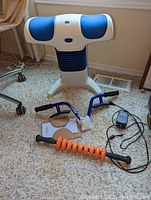 Photo of LoBak Trax back stretcher in white and blue with electric control, electric massager with blue frame and hand grips, and orange handheld roller on carpeted floor.