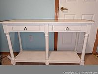 Front view of warm white sofa back console table showing two drawers with ring pulls, turned legs, and lower shelf.