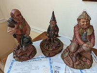 Photo showing three Tom Clark gnome statues with certificates of authenticity placed on a white cloth.