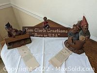 Five Tom Clark gnome ceramic figurines arranged on a white cloth including a wooden sign plaque and four gnome characters.