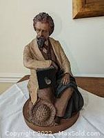 Front view of ceramic figurine depicting Matthew Brady seated, showing detailed face, clothing, and hat placement on base.