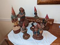 Full lot photo showing seven varied Tom Clark gnome figurines and Gnome Crossing sign on cloth-covered surface.