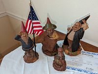 Photo showing all four Tom Clark gnome figurines displayed together with Certificate of Authenticity on a white cloth.