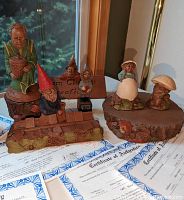 Lot showing six Tom Clark gnome figurines, wooden riser, wooden sign, and several certificates of authenticity laid out on a table near a window.