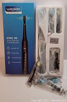 Photo shows the Wepklin ESNL 30 sonic electric toothbrush box with one handle, four toothbrush heads, USB charging cable, and packaging insert secured in white plastic tray.