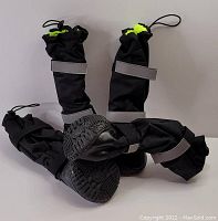 Four black fleece lined dog boots shown upright and on their sides to display soles, straps, and cinch tops with elastic cords