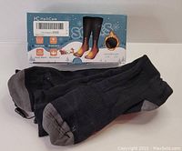 Black and gray heated socks with their original packaging box showing brand, size, and features.