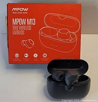 Photo of the MPOW M13 earbuds outside and inside the wireless charging case, shown with product box in background.