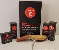 Photo shows contents of the Sminiker men's beard grooming kit including beard oil, beard balm, beard wash boxes, wooden brush, comb, and scissors arranged on a white background.