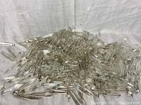 Pile of numerous clear crystal lustre chandelier prisms scattered on white fabric, showing quantity and condition.