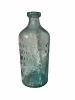 Front angle of antique glass bottle showing embossed text with light background fabric.