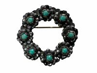 Front view of antique circular wreath pin made of sterling silver with turquoise stones arranged in flower clusters.