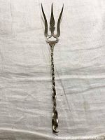 Overall view of antique sterling silver trident hors d'oeuvres fork placed flat on white cloth, showing the full length and three-pronged tip with twisted handle.