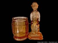 Charlie Chaplin Depression glass toothpick holder in amber, shown against a black background, side view highlighting the barrel and figure details.