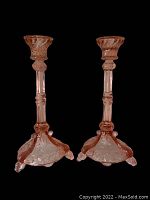 Pair of pink Depression glass candle holders with intricate embossed floral designs, viewed against black and white backgrounds.