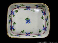 Top view of rectangular porcelain ring dish showing floral hand painted design with blue and purple flowers and green leaves on white background, with gold rim detail.