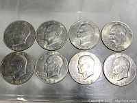 Eight Eisenhower Ike dollar coins, mostly 1972 with one 1971, displayed in two rows on a metallic surface.