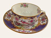 Tea cup and saucer set with purple cockatrice design by Mintons, showing side view of cup in saucer.